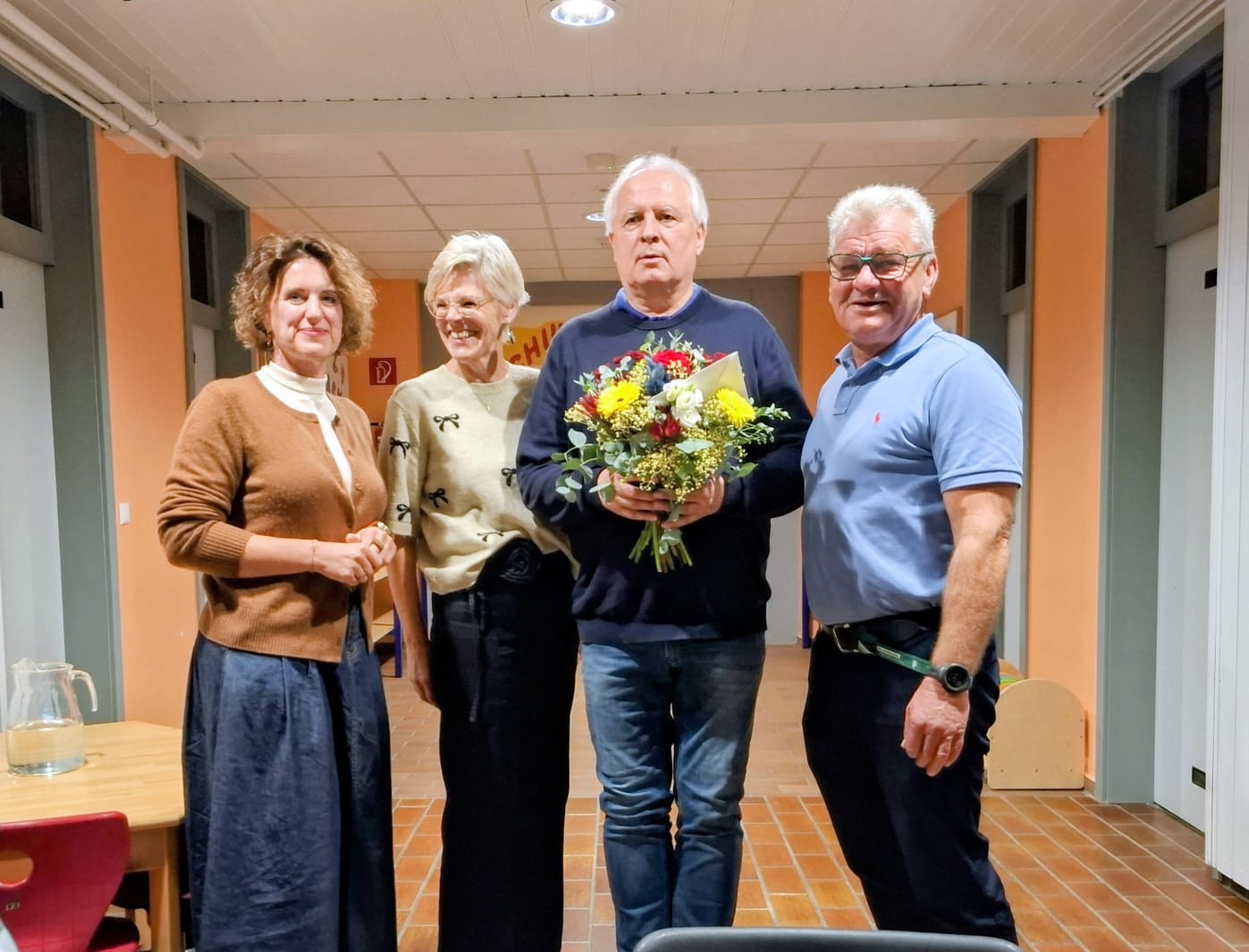 Vier Personen stehen in einem Flur, eine Person hält einen Blumenstrauß.
